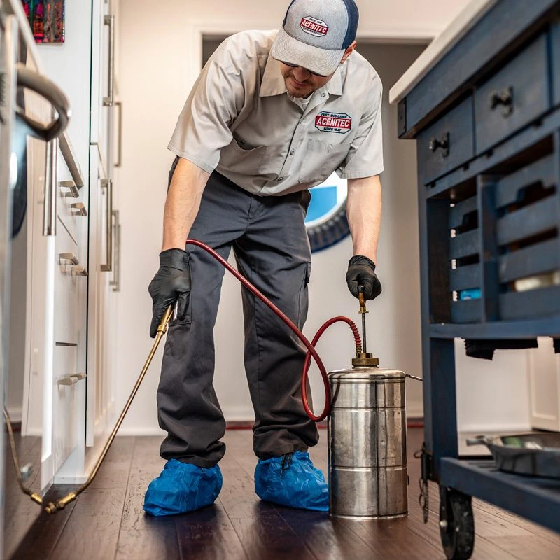 An Acenitec technician applying an interior treatment along kitchen baseboards, shoe covers on